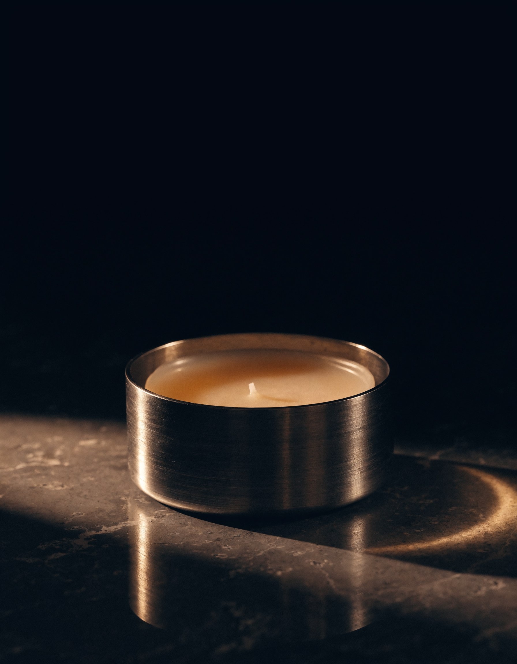 CIRE — a brushed-steel perfumed wax candle, lit taper catching amber light on dark stone.